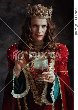 insidious medieval queen in dress pouring poison into goblet 111785809