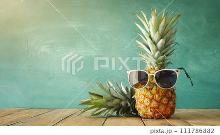 Ripe pineapple in stylish sunglasses over wooden table background. Tropical summer vacation concept. top view Ripe pineapple in stylish sunglasses over wooden table background. Tropical summer vacation concept. top view 111786882