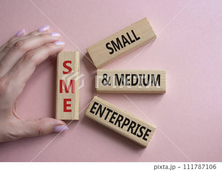 SME - Small and Medium Enterprise symbol. Wooden cubes with words SME. Businessman hand. Beautiful pink background. Business and SME concept. Copy space. SME - Small and Medium Enterprise symbol. Wooden cubes with words SME. Businessman hand. Beautiful pink background. Business and SME concept. Copy space. 111787106