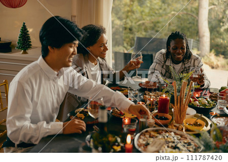 Group of smiling friends enjoying in conversation and drinking wine during Christmas party at home 111787420