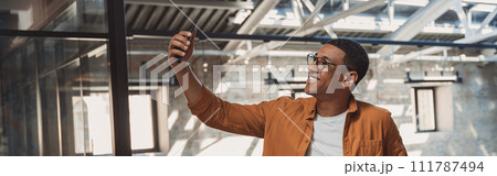 Young smiling freelancer talking by phone via video call while standing on coworking background 111787494