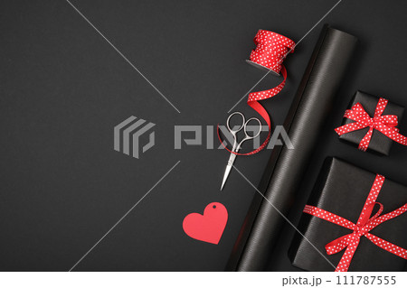 Love gift wrapping. Craft black wrapping paper, red dotted ribbon, gift tag, box, scissors. Copyspace Love gift wrapping. Craft black wrapping paper, red dotted ribbon, gift tag, box, scissors. Copyspace 111787555