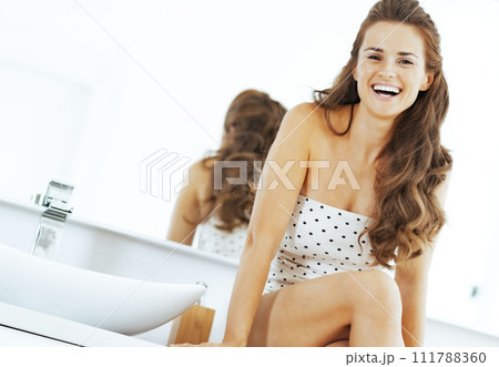 Happy young woman sitting in bathroom Happy young woman sitting in bathroom 111788360