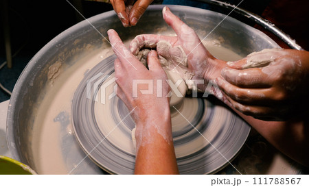A potter forms a beautiful creation out of white clay. Lessons from a master in an open class. Pottery workshop. 111788567
