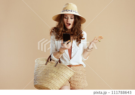 surprised trendy woman in blouse and shorts using phone 111788643
