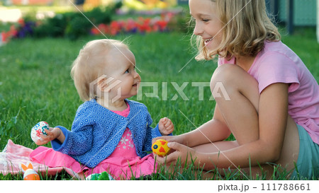 Baby girl with her sister tapping with colorful eggs on the grass at Easter Baby girl with her sister tapping with colorful eggs on the grass at Easter 111788661