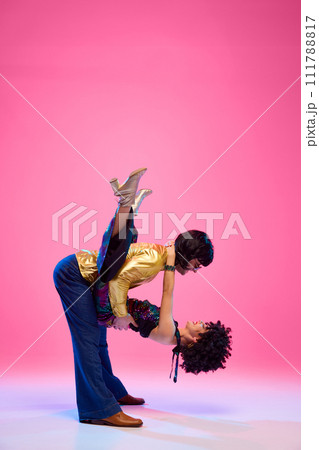 Echoes of 70s. Dance duo, female and male dancers posing in vivid retro fashion outfits against gradient pink studio background. 111788817