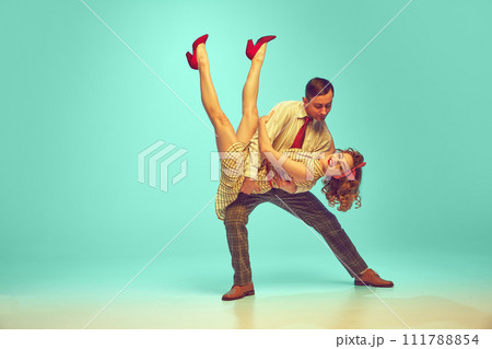 Dynamic portrait of happy couple performing lively swing dance moves in motion against gradient mint background. 111788854