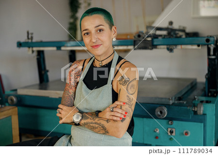Portrait of female designer standing with crossed hands on background of print machine in workshop Portrait of female designer standing with crossed hands on background of print machine in workshop 111789034