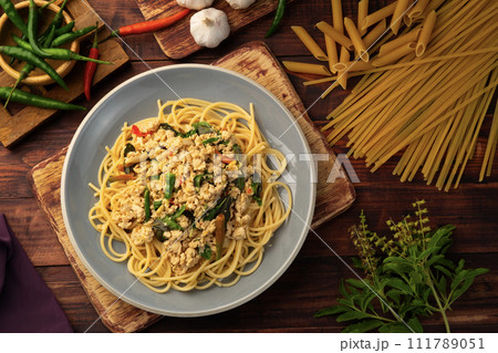 Stir fried spicy spaghetti with minced chicken breast and basil leaves in white plate,Spicy pasta Pad Kra Pao.Healthy Thai fusion food.Top view 111789051