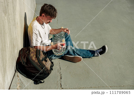 Stylish young man repairing his skateboard in the skate park. Extreme sport concept Stylish young man repairing his skateboard in the skate park. Extreme sport concept 111789065