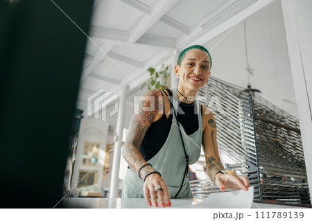 Smiling female worker preparing screen printing film while using printing machine in a workshop 111789139