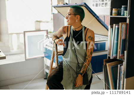 Creative female designer sitting on background of print machine in workshop Creative female designer sitting on background of print machine in workshop 111789141