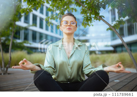 relaxed woman worker in green blouse and eyeglasses meditating 111789661