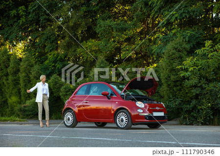 Woman raising her finger stops drivers for help standing near car with open hood Woman raising her finger stops drivers for help standing near car with open hood 111790346