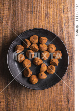 Chocolate truffles covered with cocoa powder on plate on wooden table. Top view. 111792242