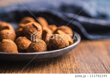 Chocolate truffles covered with cocoa powder on plate on wooden table. 111792245