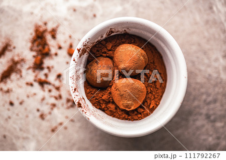 Chocolate truffles covered with cocoa powder in bowl on kitchen table.Top view. Chocolate truffles covered with cocoa powder in bowl on kitchen table.Top view. 111792267