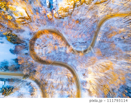 Winding asphalt road in sunny winter morning. Cold and freezy forested countryside.. Aerial view from drone. Winding asphalt road in sunny winter morning. Cold and freezy forested countryside.. Aerial view from drone. 111793114