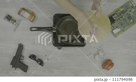 Man cooks meat in a frying pan. Man prepares the ham in the pan, on the table are: gun, glasses, chip and pepper, the abstraction for instagram a plate 111794096