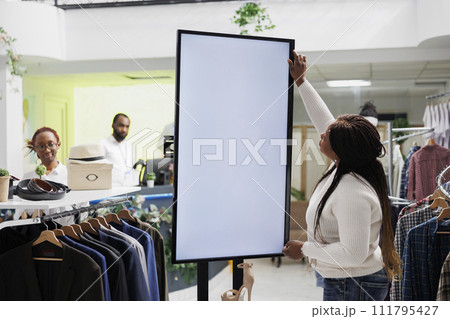 Boutique customer browsing footwear on white blank digital screen in shopping center. African american woman examining shoes brand new collection using interactive whiteboard in store 111795427