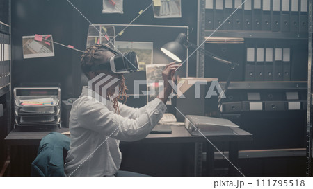 Young investigator using 3d vr headset in incident room, using interactive virtual reality glasses to uncover new clues. Police agent checking forensic evidence and doing detective work. 111795518