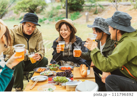 キャンプ・デイキャンプ・グループキャンプでビールを飲みながら談笑する男女キャンパー 111796892