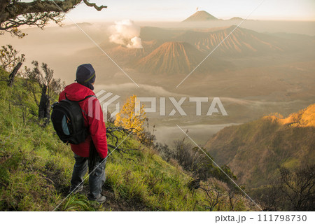 Back view of tourist standing on the hill and looking to the beautiful sunrise of Bromo Tengger Semeru National Park in East Java, Indonesia. Back view of tourist standing on the hill and looking to the beautiful sunrise of Bromo Tengger Semeru National Park in East Java, Indonesia. 111798730