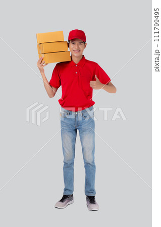 Young asian man in uniform red and cap carrying box stack and gesture thumbs up isolated. Young asian man in uniform red and cap carrying box stack and gesture thumbs up isolated. 111799495