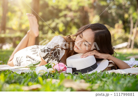 A carefree Asian woman is falling asleep or taking a nap on a picnic mat in a park. 111799881