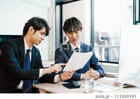 屋外で手帳を広げ真剣な表情で内容を確認する20代のスーツの男性1人 111800595