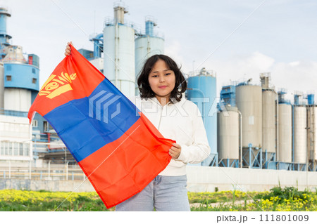 Happy young woman with flag of Mongolia against background of factory 111801009