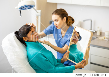 Beautician examining face skin of female patient Beautician examining face skin of female patient 111801031