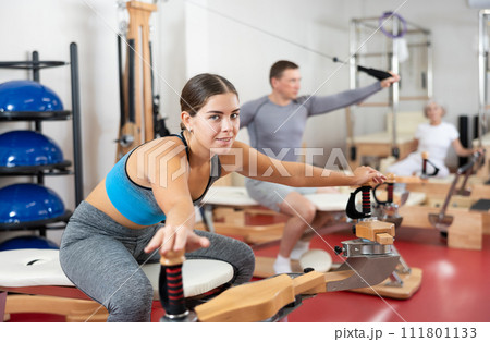 Young woman stretching her arms using pilates machine Young woman stretching her arms using pilates machine 111801133