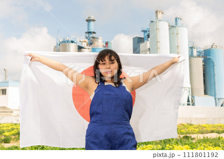 Worried asian girl in work clothes with flag of japan standing in front of industrial scenery Worried asian girl in work clothes with flag of japan standing in front of industrial scenery 111801192