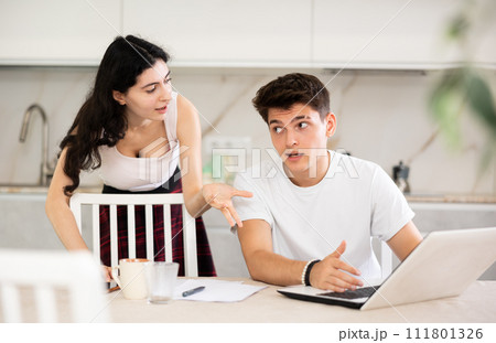 Sad freelancer husband works at home on laptop and listens to her wife reproaches in frustration. Sad freelancer husband works at home on laptop and listens to her wife reproaches in frustration. 111801326