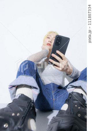 ストリートファッションを着て座ってスマホを持つ金髪の若い女性 111807334