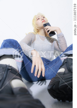 ストリートファッションを着て座ってスマホを持つ金髪の若い女性 ストリートファッションを着て座ってスマホを持つ金髪の若い女性 111807339