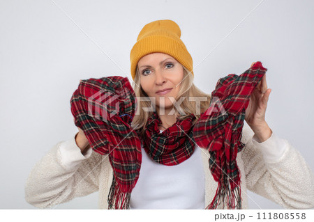 Close-up portrait of an elderly woman in a knitted hat, wrapped in a scarf against the cold on a gray background 111808558