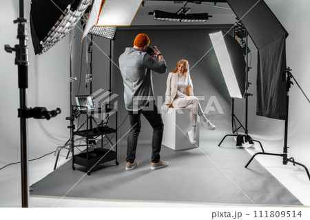 Man photographing woman sitting on cube in photo studio Man photographing woman sitting on cube in photo studio 111809514