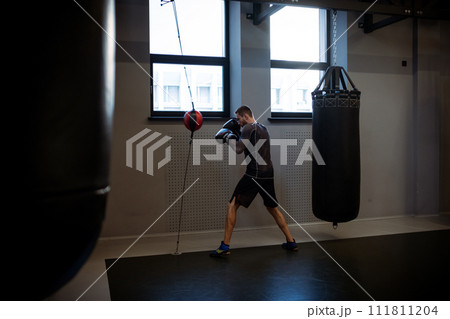 Man in boxing gloves training with floor to ceiling bag 111811204
