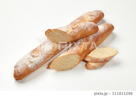 Closeup of freshly baked whole and sliced wheat baguettes isolated on white background. Main staple. Artisanal breadmaking concept Closeup of freshly baked whole and sliced wheat baguettes isolated on white background. Main staple. Artisanal breadmaking concept 111811298