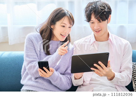 スマートフォンとタブレットPCの画面を見比べる男女 111812036