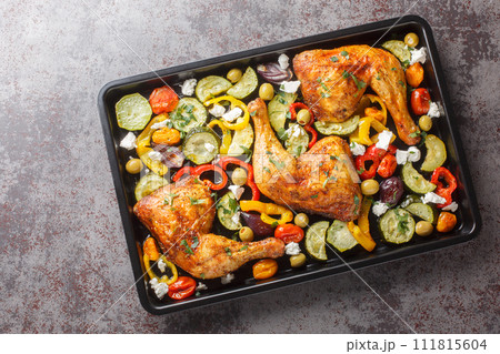 Delicious Mediterranean baked chicken legs with vegetables and feta cheese close-up on a baking sheet on the table. Horizontal top view Delicious Mediterranean baked chicken legs with vegetables and feta cheese close-up on a baking sheet on the table. Horizontal top view 111815604