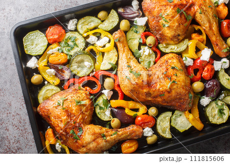 Greek style baked chicken quarters with zucchini, tomatoes, peppers, olives and feta cheese close-up on a baking sheet. Horizontal top view 111815606