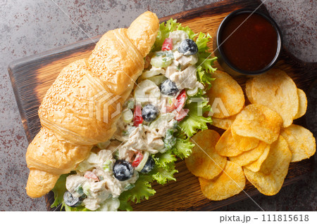 Closeup of a chicken salad and lettuce sandwich on a croissant roll with potato chips on a wooden board. Horizontal top view Closeup of a chicken salad and lettuce sandwich on a croissant roll with potato chips on a wooden board. Horizontal top view 111815618