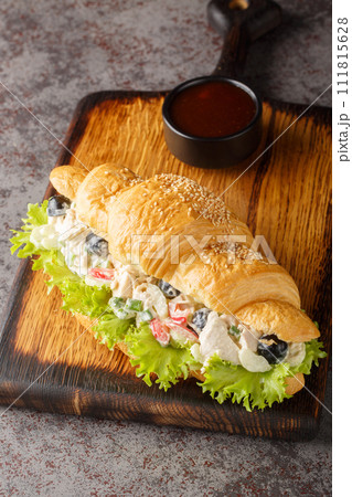 Croissant sandwich with salad made from chicken, grapes, onions, celery, dressed with mayonnaise close-up on a wooden board. Vertical Croissant sandwich with salad made from chicken, grapes, onions, celery, dressed with mayonnaise close-up on a wooden board. Vertical 111815628