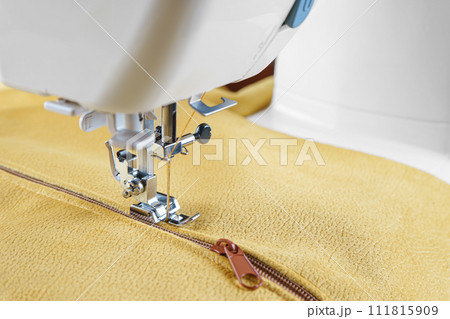 Modern sewing machine with special presser foot on yellow velours fabric close up Modern sewing machine with special presser foot on yellow velours fabric close up 111815909