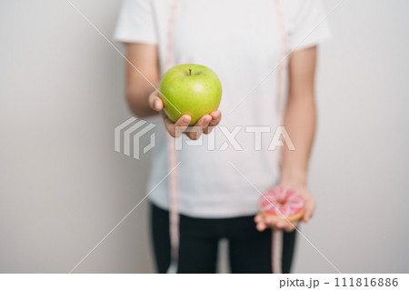 woman hand hold green Apple and donut, female fitness choose between fruit is Healthy and sweet is Unhealthy junk food. Dieting control, Weight loss, Obesity, eating lifestyle and nutrition concept woman hand hold green Apple and donut, female fitness choose between fruit is Healthy and sweet is Unhealthy junk food. Dieting control, Weight loss, Obesity, eating lifestyle and nutrition concept 111816886