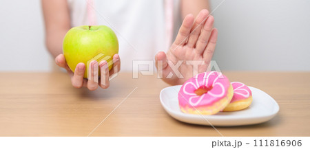 woman hand hold green Apple and reject donut, female fitness choose between fruit is Healthy and sweet is Unhealthy junk food. Dieting control, Weight loss, Obesity, eating lifestyle and nutrition woman hand hold green Apple and reject donut, female fitness choose between fruit is Healthy and sweet is Unhealthy junk food. Dieting control, Weight loss, Obesity, eating lifestyle and nutrition 111816906